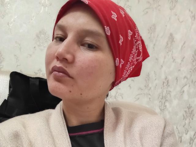 LenaEtty with a red bandana, light brown skin, small moles on her face, wearing a beige sweater over a black shirt, looking slightly to the left.