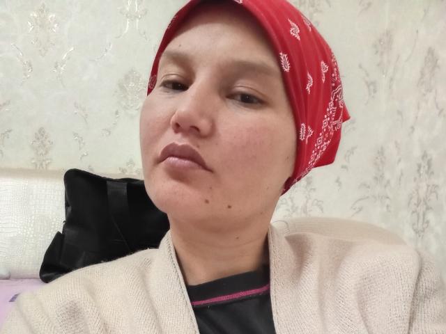 LenaEtty with a red bandana, beige knit cardigan, and black shirt, looking slightly bored with her lips closed. Her face has a small mole near her chin.