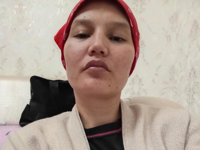 LenaEtty with a red bandana, beige sweater, and black shirt, looking straight at the camera with a neutral expression, showing small moles on her face.