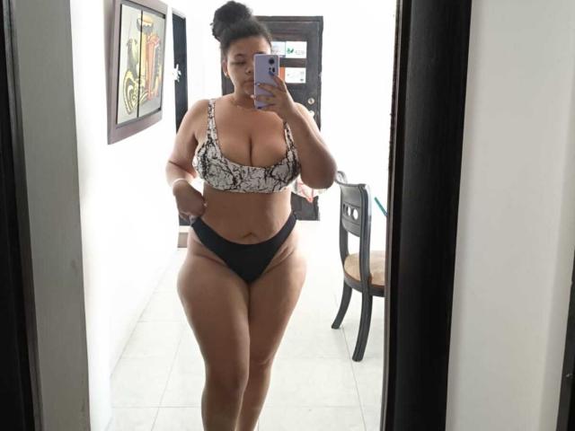 ValeriiPark with large, round, curvy tits and thick, wide ass, wearing a snake-print bra and black panties, taking a mirror selfie with a phone, black hair in a bun.