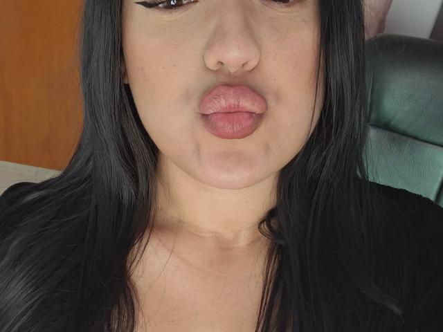 LauraRichis with puffy, pinkish-brown lips, black straight hair, and black eyeliner, making a pouty face, showing a slight chin and neck. Her nose is centered.