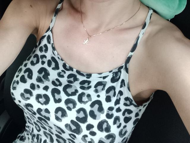 BellaJulls' tits in a leopard-print tank top, showing a slim, pale, chest with small, white necklace, and a slight tan line. Her arm and shoulder are visible.