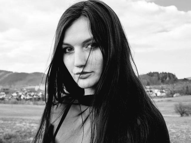 Black-and-white photo of AdelineCreazy with long, dark, wet hair, looking serious, holding a single hair in her mouth, wearing a sheer top, showing small, perky tits.
