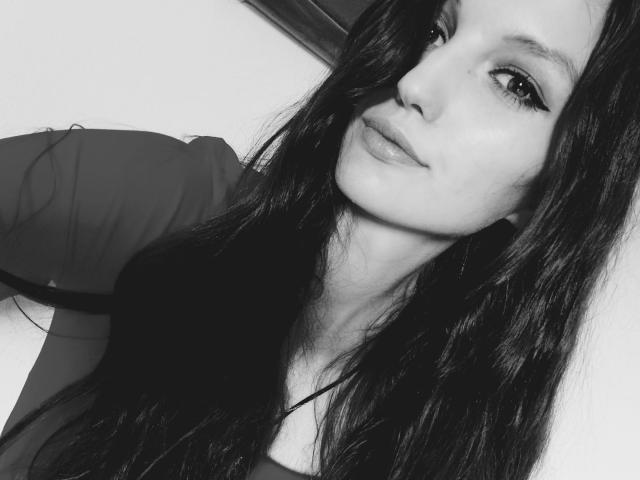 AdelineCreazy's face, black and white selfie, long dark hair, slight smile, subtle makeup, eyeliner, soft eyes, light skin, slight chin, upper body, shirt sleeve, confident expression.