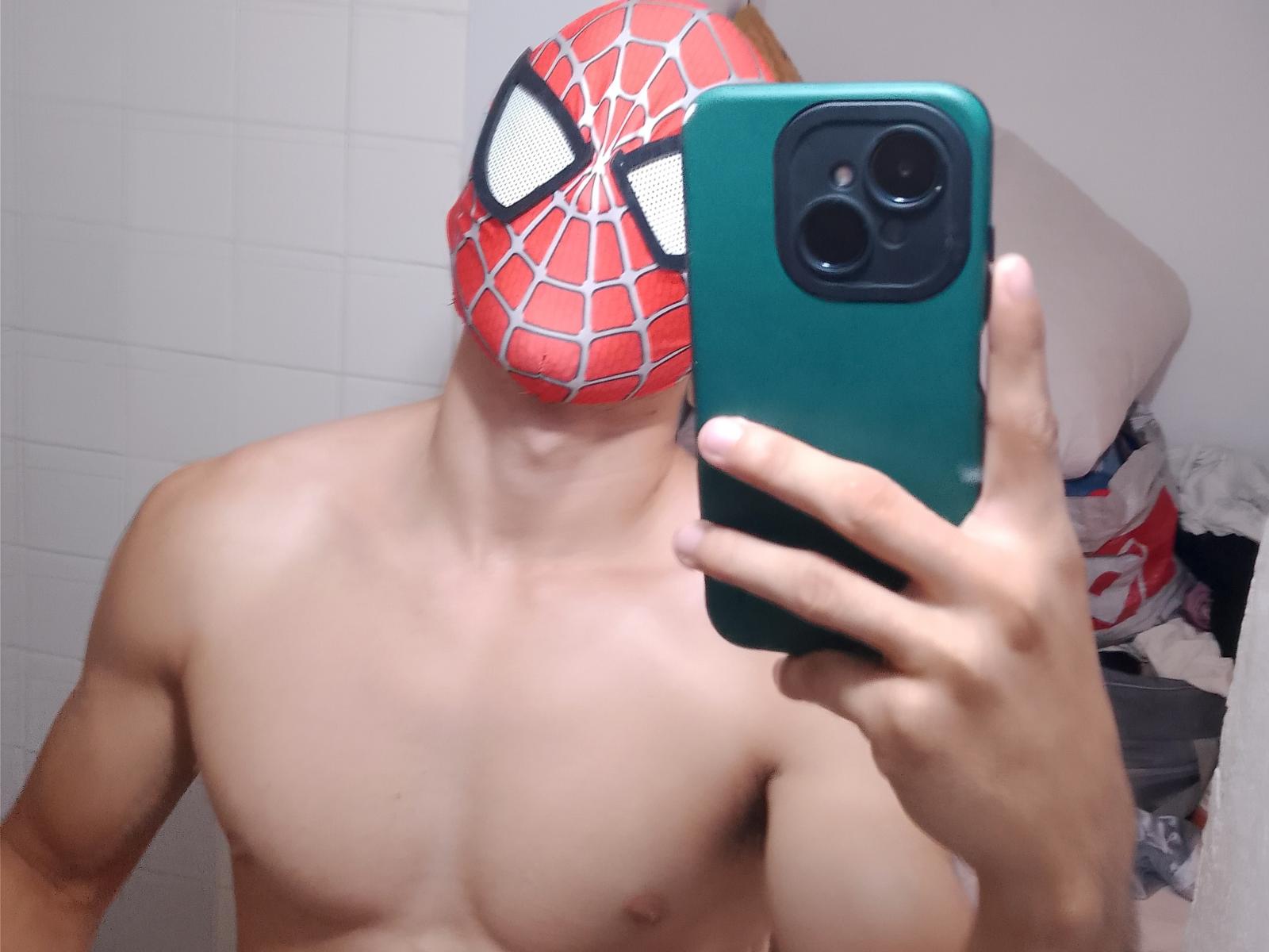 JhonnyTunder, sem camisa, usando uma máscara vermelha do Homem-Aranha com olhos brancos, tirando uma selfie com um telefone verde, com o peito e os braços visíveis, em um banheiro..