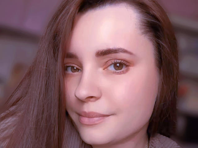TiffanyKeli a les yeux marron, une peau claire et des cheveux bruns, avec un léger sourire, des lèvres roses délicates et un nez, sur une photo de profil légèrement floue avec un éclairage doux..