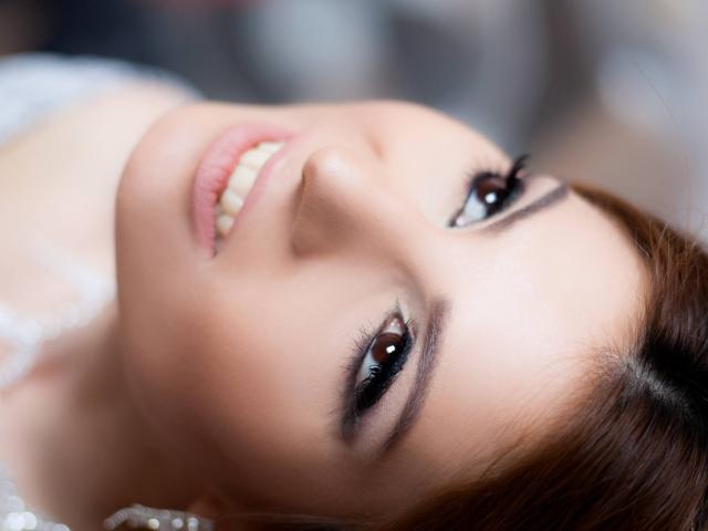 O rosto de Sexydollhotx, olhos castanhos, sorrindo com dentes brancos, pele clara e lisa, cabelo castanho, maquiagem discreta, close-up, levemente inclinado, olhando para cima, luz suave, expressão gentil..