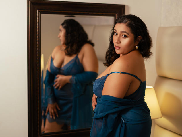 ViickyLee stands in front of a mirror, wearing a blue lace lingerie set, with her tits slightly visible, and a sheer robe off her shoulders, looking seductive.