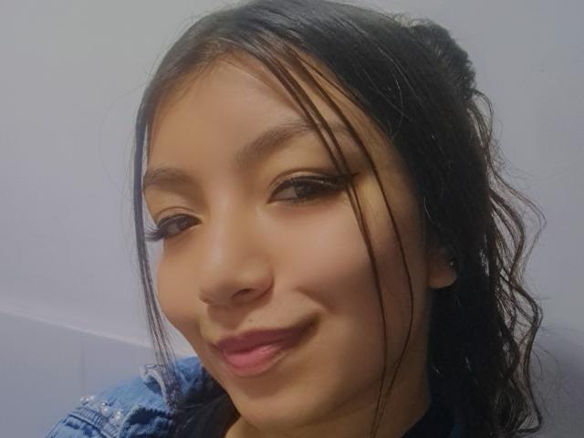 IbbyeMoreau's face, brown skin, black hair in messy bun, wearing denim jacket, slightly smiling, pink lipstick, long eyelashes, small nose ring, cute, attractive, feminine.