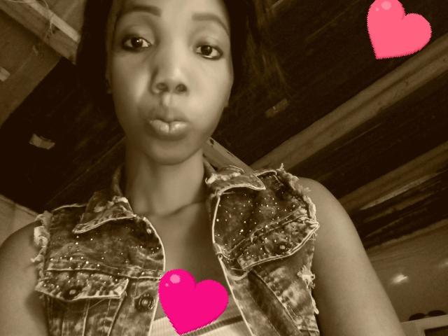 Sexytinny-hot with puffy lips, wearing a studded denim vest, has pink heart emojis covering her tits and lower ass. Brown-eyed, black-haired, medium skin tone, indoor shot.