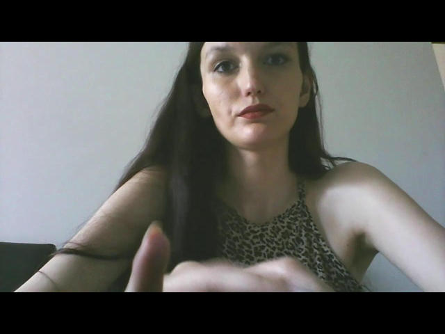 Adeline, com cabelos longos e escuros, vestindo uma blusa com estampa de leopardo, tem pele clara e batom vermelho, e está fazendo um gesto de apontar com a mão direita..