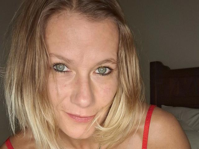 xcYola-hot has blonde hair, blue eyes, and a slight smile, wearing a red tank top, showing her face and upper chest in a selfie.