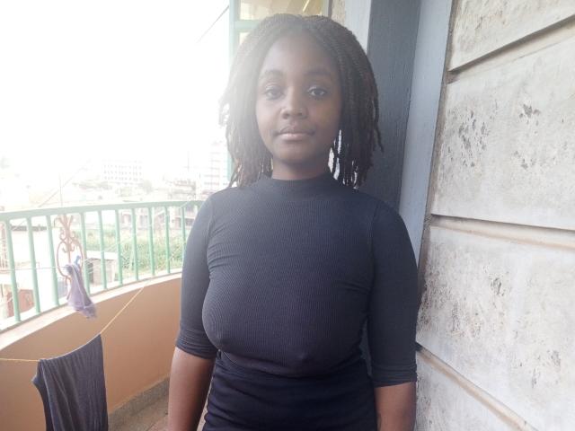 TinySnack has dark skin, medium-length black dreadlocks, and is wearing a tight black shirt that shows her small, perky tits. She's standing on a balcony with laundry.