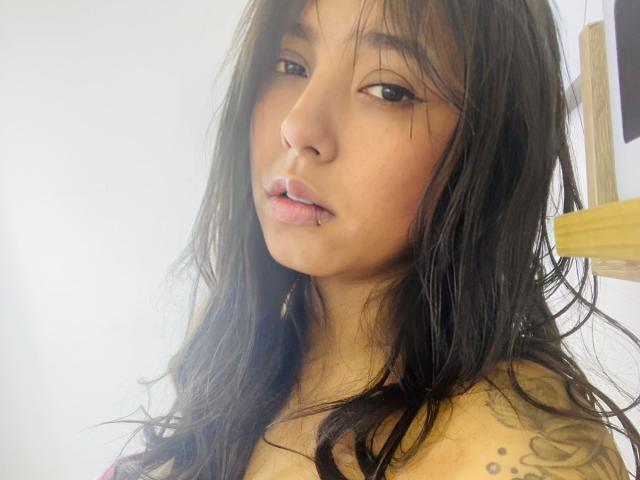 SarahMoon69 with wet black hair, slightly parted pink lips, and a tattoo on her right shoulder, looking at the camera with a subtle, sexy expression.