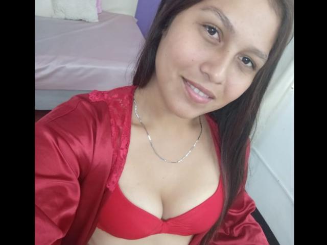 ValentinaMoreau with long brown hair, smiling, wearing a red satin robe over a red bra, showing her boobs, silver necklace, and pale skin, in a selfie.