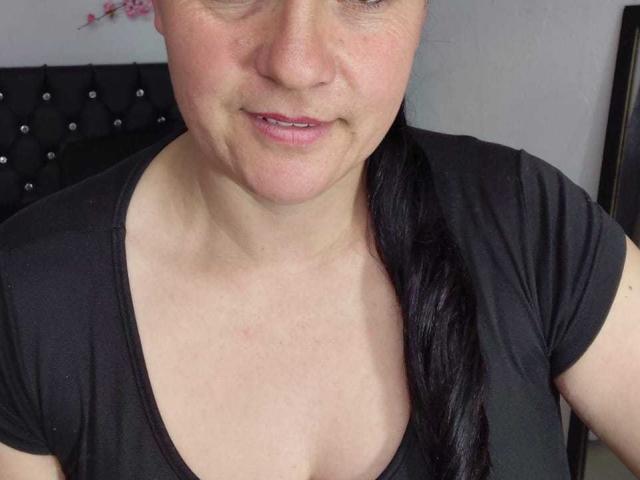 SofiaLorna a la peau pâle, un léger sourire, une queue de cheval noire, et porte une chemise noire à col en V. Ses petites seins sont à peine visibles sous la chemise..