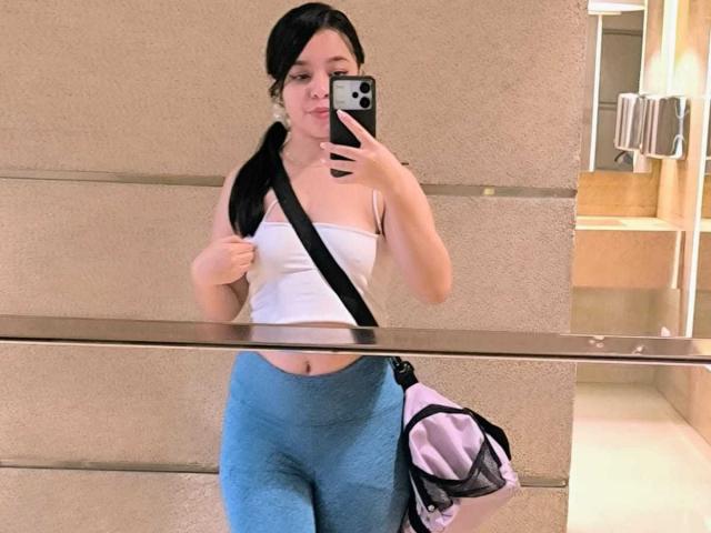 LissyCarter with black pigtails, white strapless top, blue high-waisted leggings, black crossbody bag, holding phone, mirror selfie, pink bag hanging. Boobs covered by top, ass covered by leggings.