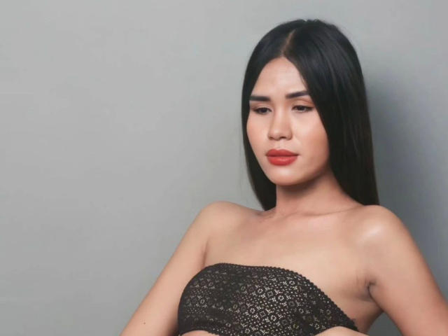 MariaPeters-hot with long black hair, wearing a black lace strapless top, has red lipstick, and a serious expression, showing bare shoulders and a small amount of cleavage.