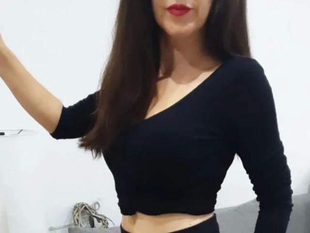 AriaDulce-hot with long brown hair, red lipstick, black long-sleeve crop top, showing midriff, arm raised, black bottoms, no visible tits or pussy.