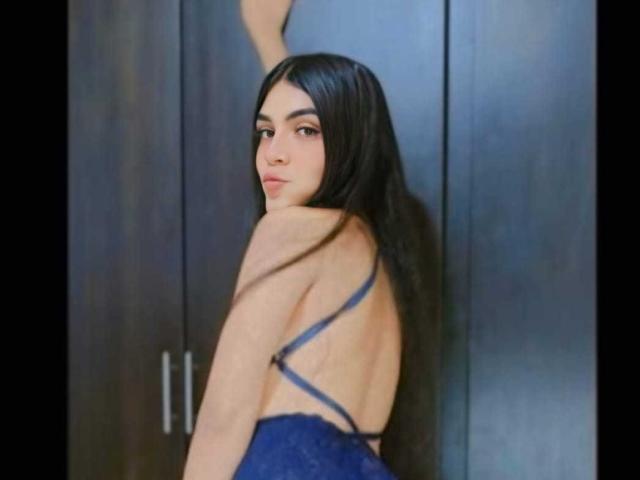 GoodCuteLadies with long black hair, blue lace dress, back exposed, looking over shoulder, arm against dark wooden door. Her tits are small, face is pretty, expression is calm.