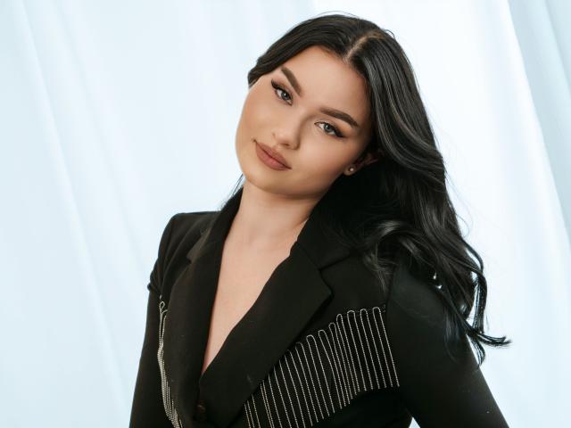HopeForLove with long black hair, wearing a black pinstriped blazer, has a subtle smile, light makeup, and a confident look. Her tits are slightly visible under the jacket.