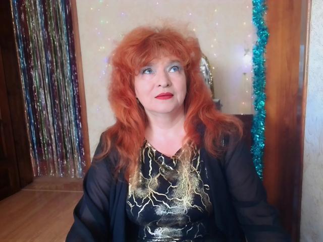 LadaMay with red curly hair, blue eyes, red lipstick, black sheer robe, and gold-patterned dress, looking up with a surprised expression, showing her tits slightly.