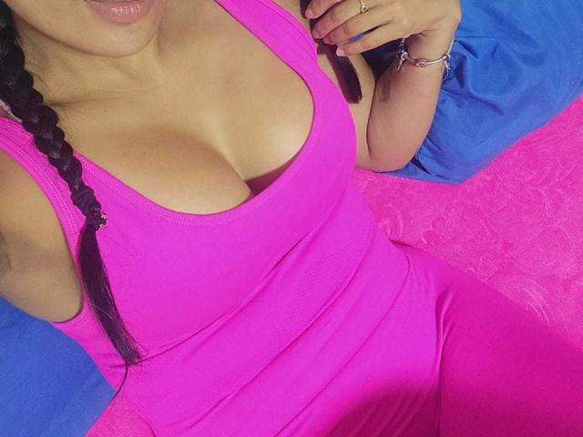 TamaraOriz has large tits in a tight pink tank top and matching pink pants, with a black braid and pink bracelet, lying on blue and pink pillows.
