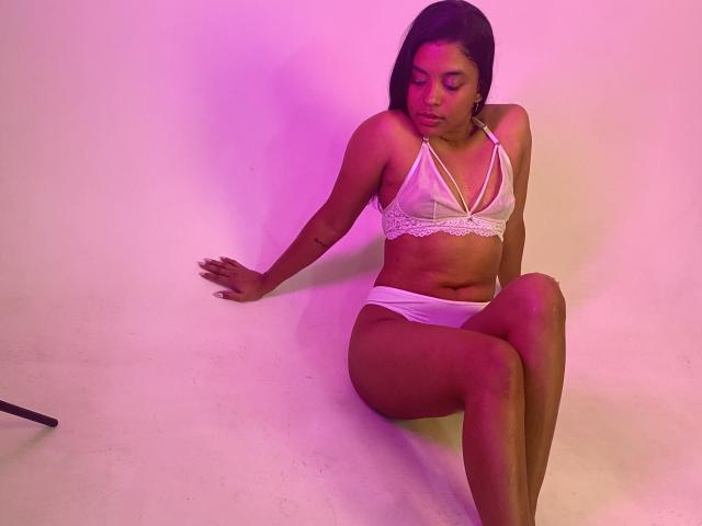 HilaryCook sitting on the floor with her back against a wall, wearing a white lace bra and white panties, her ass slightly raised, eyes closed, and arms resting.