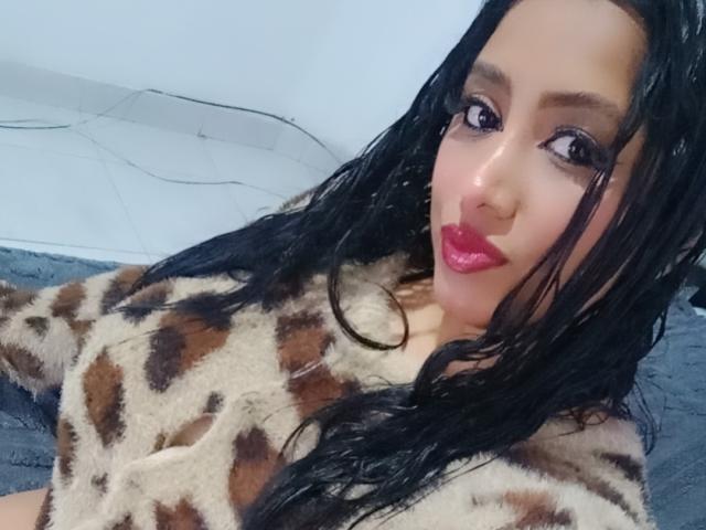 María Catalina, con el cabello negro y húmedo, lleva una blusa suave de estampado de leopardo, tiene un brillo labial rosa y delineador de ojos oscuro, y mira a la cámara con una ligera sonrisa. Se pueden ver sus senos..