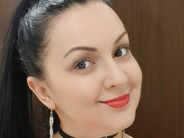 LoraHazel has a cute face, dark brown eyes, black ponytail, red lipstick, and diamond earrings, smiling with a light skin tone and a black choker.