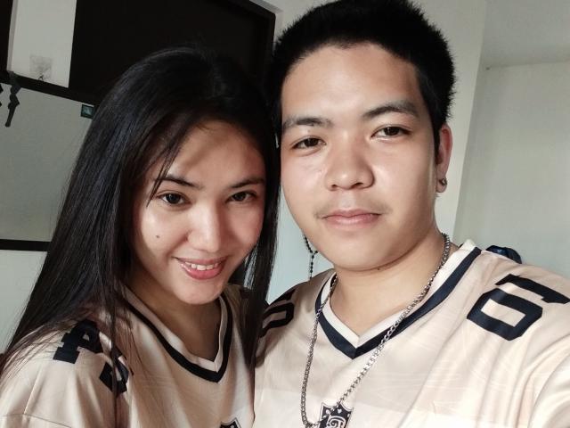AsianCoupleDesire présente une femme asiatique souriante, avec de longs cheveux noirs et de petites seins, debout à côté d'un homme asiatique corpulent, avec des cheveux noirs courts et un collier..