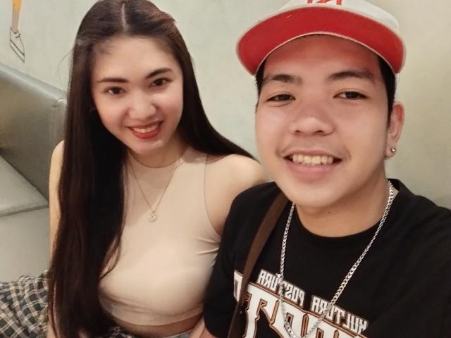 Couple asiatique, femme asiatique aux longs cheveux noirs, rouge à lèvres rouge, crop top beige, montrant ses seins, souriante. Homme asiatique, casquette rouge et blanche, chemise noire, chaîne, souriant, montrant ses dents..