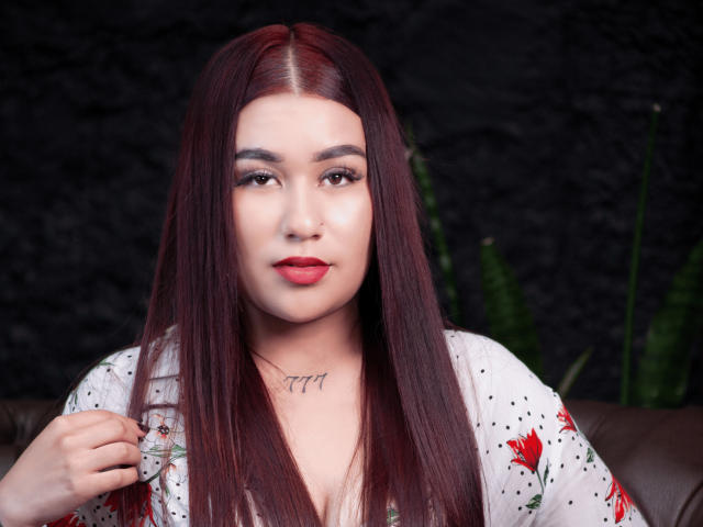 Valeria Torrez tiene el pelo largo y rojo, lápiz labial rojo y un tatuaje debajo del mentón. Lleva una camisa con estampado floral, sostiene un anillo, tiene los ojos marrones y una sonrisa sutil..