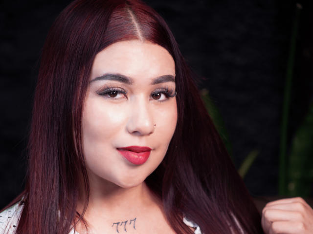 ValeriaTorrez tem cabelo ruivo, pele clara e batom vermelho. Ela usa delineador escuro, tem um piercing no nariz e uma tatuagem abaixo do queixo. Seus seios estão levemente visíveis..