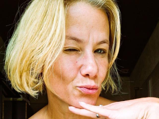xcYola-hot with blonde bob, winking, and puckering lips, hand touching chin, wearing a ring, has light skin, and a small mole on her right cheek.