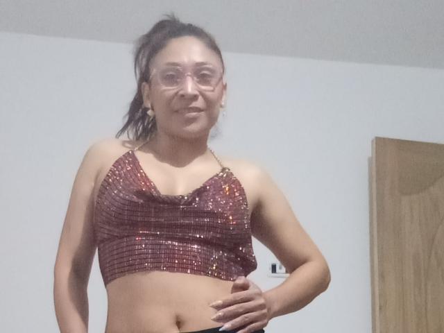 PalomaSexyBeauty, a sexy Latina woman with glasses, wearing a sparkly red sequin crop top, has her hand on her hip, showing her tits and a slight smile.