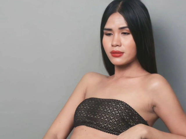 MariaPeters-hot with long black hair, wearing a black lace tube top, exposing her bare tits, has a light skin tone, red lipstick, and a neutral expression.