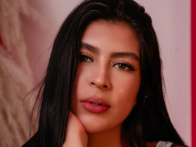 SamanthaEva69 has long black hair, golden glittery eyes, pinkish-red lips, and a slightly flushed face, with her hand touching her neck, looking directly at the camera.