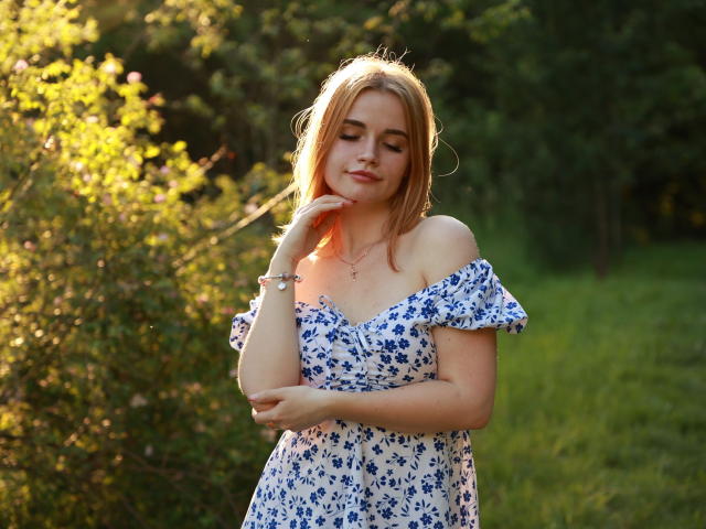 MargaritaKis has blonde hair, blue floral dress, off-shoulder, cute, small tits, hand on cheek, green background, sunlight, relaxed, bracelet, necklace, smiling, standing, outdoors, summer.