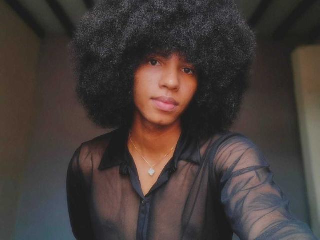 AntonyCarterr has a big, fluffy black afro and is wearing a sheer black button-up shirt, showing a small, cute, brown ass through the fabric.