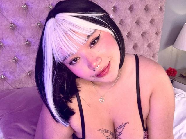 HonnyBlaice's big ass in black thong, kneeling on a bed, with purple lighting. Her hand rests on her thigh, showing off her curvy, voluptuous butt.