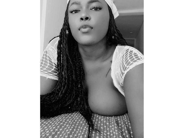 MacarenaBoobs has dark skin, long braided hair, and wears a lace top exposing her tits. She's looking at the camera with pouty lips in a black-and-white photo.