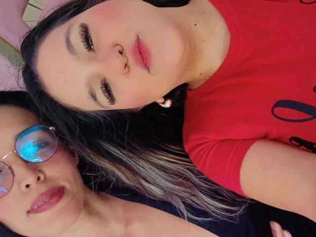 JenniferAndMia with nose ring, red shirt, and long black/gray hair, next to Mia with blue reflective glasses, black shirt, and nose ring, both looking at camera.