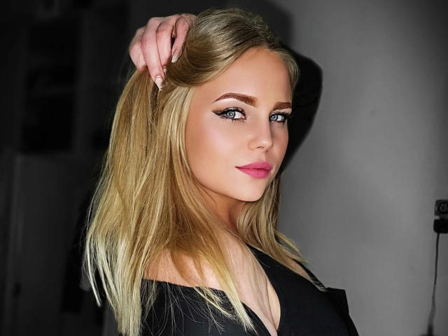 CherryDeluxe-hot with blonde hair, blue eyes, pink lipstick, black off-shoulder top, hand in hair, sexy look, sharp makeup, medium breast size, soft smile, attractive, confident.
