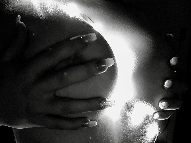CherryDeluxe-hot's hands are cupping her bare, large, shiny tits with well-manicured nails in a black-and-white, high-contrast photo.
