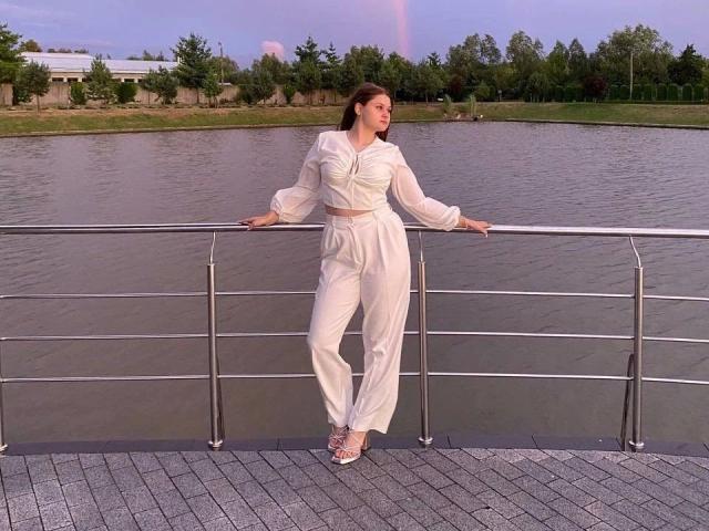 BellaMuse-hot in white puffy-sleeve pantsuit, standing on a metal railing, hands on rail, looking to the side, wearing white strappy sandals, by a calm river.