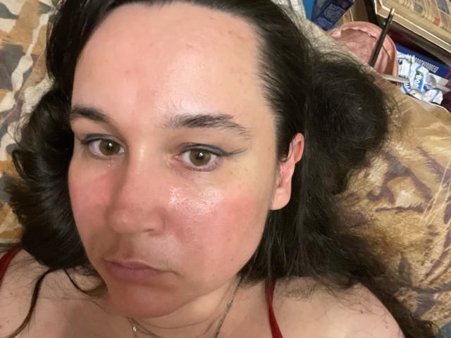 SaliBerry has a chubby face with pinkish skin, brown eyes, black wavy hair, and is lying down with a serious expression, wearing a red top.