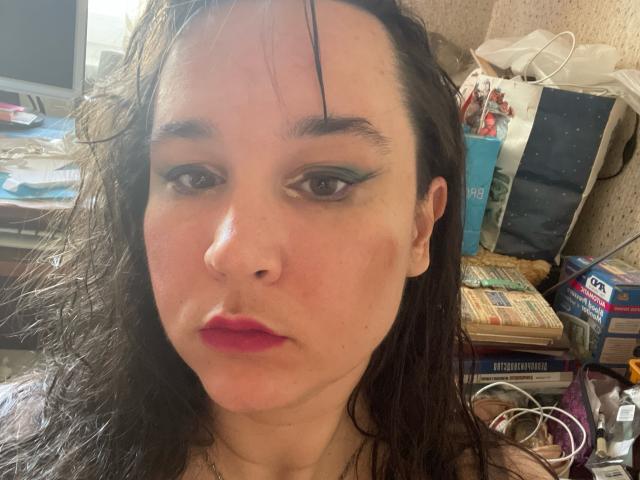 SaliBerry has wet dark hair, green eyeliner, pink lipstick, and a serious expression. Her nose is small and she has light skin with a few freckles. Boobs not visible.