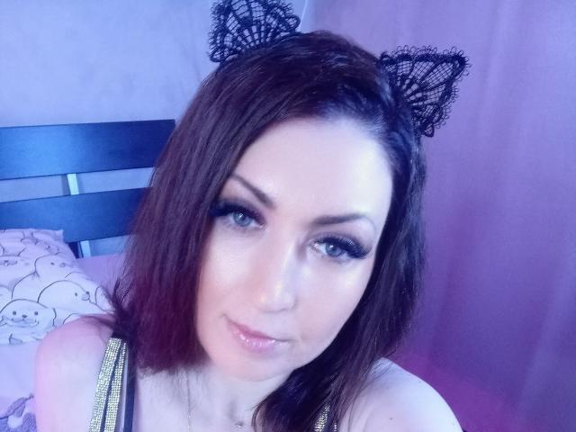 WikiStar met donkerbruin haar, kattenoren en blauwe ogen, die lichtjes glimlacht, met gouden bandjes, blauwe eyeliner en roze lippenstift, en die naar de camera kijkt..