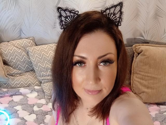 WikiStar con orecchie da gatto, capelli castani e labbra rosa lucide, indossa una maglietta rosa, ha grandi occhi azzurri e un leggero sorriso, appare carina e sensuale..